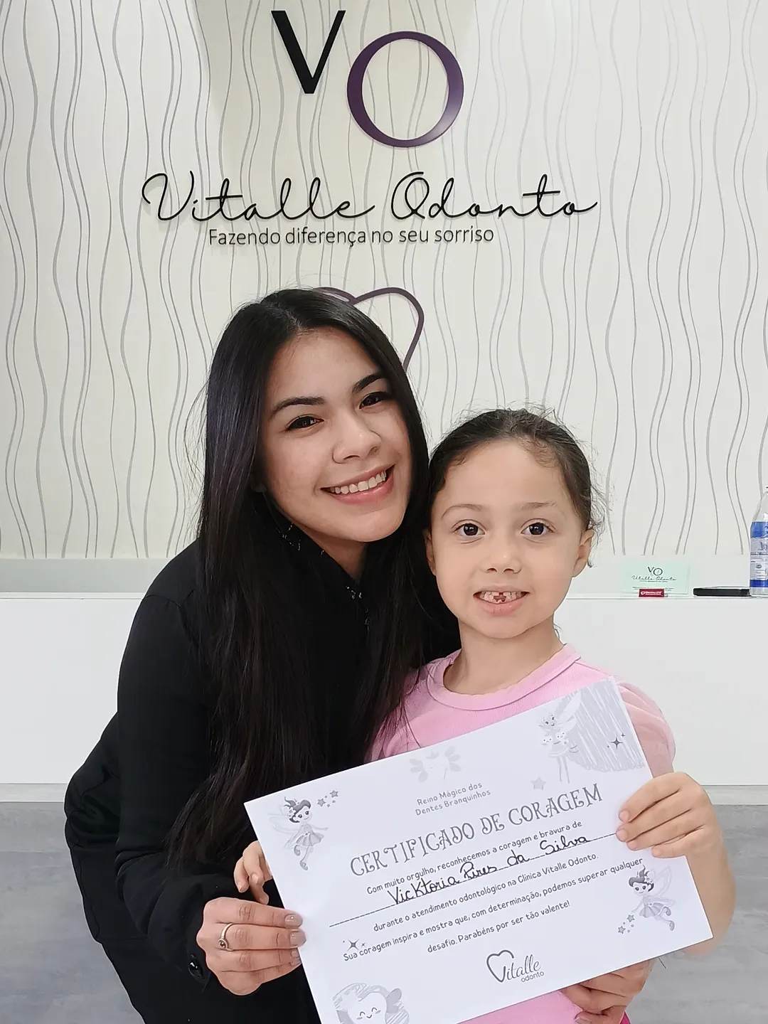 Colaboradora da Vitalle Odonto com paciente infantil, em frente à parede de marca da clínica